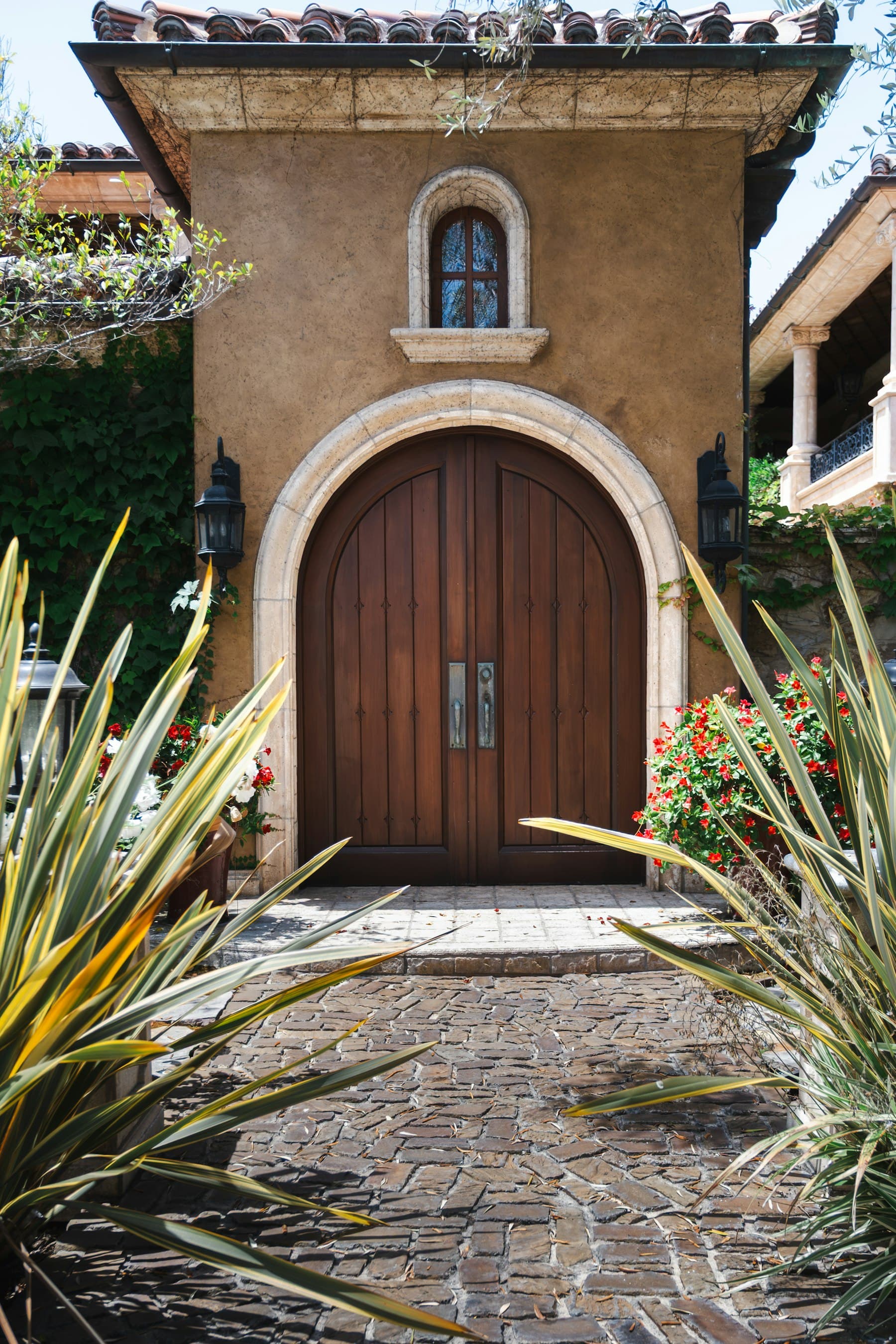 Arched wooden double doors of a Mediterranean-style home framed by tropical plants